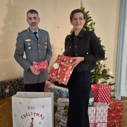 Oberstapotheker Martin Melcher und Dr. Ariane Körner stehen vor einem geschmückten Weihnachtsbaum mit Geschenken und halten Päckchen in den Händen.