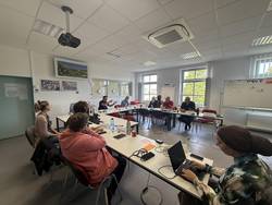 Cyberangriff-Übung im Burgenlandkreis © Pressestelle Burgenlandkreis Teilnehmende der Cyberangriff-Krisenübung des Burgenlandkreises arbeiten konzentriert an Laptops in einem Besprechungsraum. Im Hintergrund stehen Mitarbeitende des Gesundheitsamts und des Amtes für Bevölkerungsschutz vor einer großen Leinwand und einer Einsatzkarte.