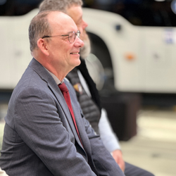 Lutz Däumler, langjähriger Geschäftsführer der PVG, bei seiner Verabschiedung in den Ruhestand, im Vordergrund lächelnd im grauen Anzug mit roter Krawatte.