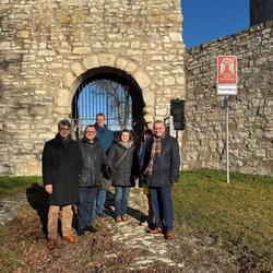 Vertreter der Kulturstiftung Sachsen-Anhalt, des Burgenlandkreises und der Stadt Eckartsberga stehen gemeinsam vor dem Burgtor der Eckartsburg. Im Hintergrund ist das Tor mit Gitter und ein Schild zur „Straße der Romanik“ sichtbar. Das Treffen fand im Rahmen der geplanten Sanierung und Teilöffnung der Burg statt.