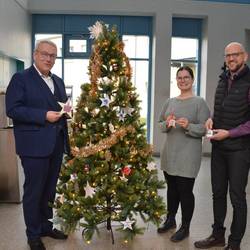 Landrat Götz Ulrich, Personalratsvorsitzender Ronny Just und Heimleiterin Lisa Stieber (v.l.) stehen an dem Wünschebaum im Landratsamt Naumburg.