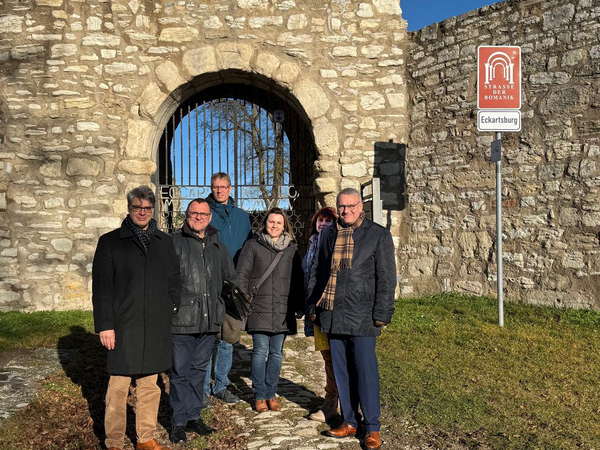 Vertreter der Kulturstiftung Sachsen-Anhalt, des Burgenlandkreises und der Stadt Eckartsberga stehen gemeinsam vor dem Burgtor der Eckartsburg. Im Hintergrund ist das Tor mit Gitter und ein Schild zur „Straße der Romanik“ sichtbar. Das Treffen fand im Rahmen der geplanten Sanierung und Teilöffnung der Burg statt.